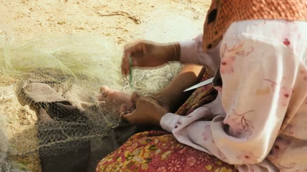 Close-up on a woman sitting down on the riverbank to mend a fishing net by hand — Stock Video