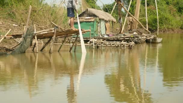 Рыбак вытаскивает сеть из воды, стоя на маленькой бамбуковой платформе . — стоковое видео