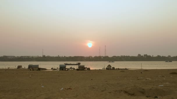 Vue à distance du petit village de pêcheurs avec des maisons en échasses sur le bord de la rivière au coucher du soleil. Barge descendant la rivière comme toile de fond — Video
