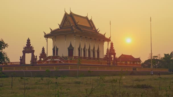 Un par de jóvenes montando en bicicleta más allá de un recinto de pagoda al atardecer — Vídeo de stock