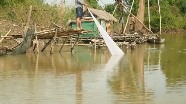 Pescatore sta tirando la rete fuori dall'acqua in piedi su una piccola piattaforma di bambù . — Video Stock