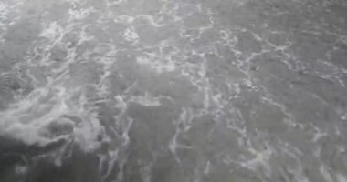 Çalkantılı beyaz köpükleri kumsalda sağanak yağış sırasında çamurlu suyu kaplıyor..