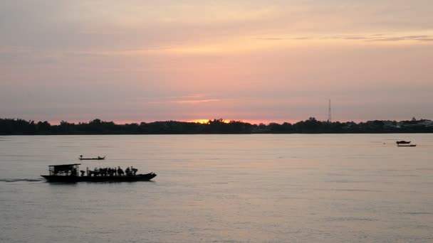 Barco de balsa cruzando o rio ao nascer do sol com a silhueta de pequenos barcos de pesca como pano de fundo — Vídeo de Stock