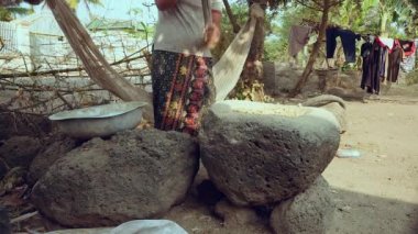Woman pounding food using a wooden pestle with handle in a large stone mortar