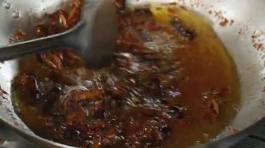 Metal bir spatula kullanarak bir wok içinde derin kızartma çekirge karıştırarak kadın