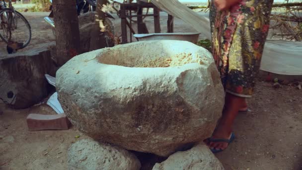 Woman pounding food using a wooden pestle with handle in a large stone mortar — ストック動画