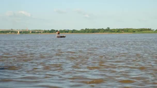 Pescador remando su pequeño barco en el río mientras tirando de una red de pesca a través del agua detrás — Vídeos de Stock