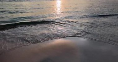 Altın bir günbatımında yumuşak kumların üzerinde hafif dalgalar süzülüyor. (yavaş çekimde )