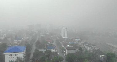 Düşük görüş mesafesi ve soluk binaları olan yağmurlu şehir manzarası.