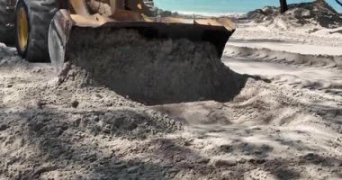 Ön uçtaki yükleyiciyi kapatır plaj boyunca kum yığınını iter, metal kovası sıkı çalışır..