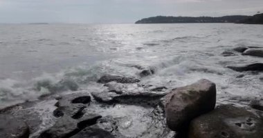 Okyanus dalgaları engebeli, kayalık bir kıyı şeridine çarpıyor, beyaz köpük ve sprey püskürtüyor..