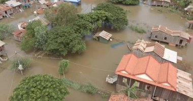 Geleneksel evlerin kısmen bulanık sulara gömüldüğü su basmış bir Kamboçya köyünün hava manzarası..