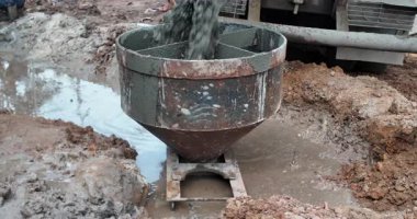 Çamurlu bir şantiyede ıslak betonla doldurulan büyük metal zıpzıp.
