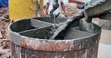 Çamurlu bir inşaat sahasında ıslak betonla doldurulan büyük bir metal zıpzıpzıpın yakınına.