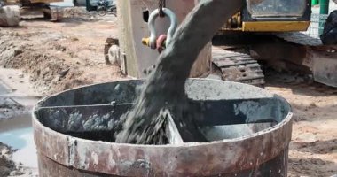 Çamurlu bir inşaat sahasında ıslak betonla doldurulan büyük bir metal zıpzıpzıpın yakınına..