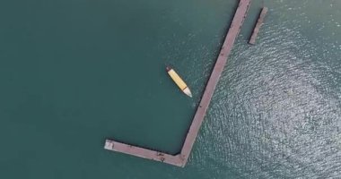 Işıldayan turkuaz bir denizde, L şeklinde bir iskelede geleneksel bir motorlu teknenin yukarıdan aşağı hava görüntüsü..