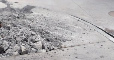 Paslı bir kazıcı kovasını kapatın. Kalın bir beton kaldırımı delip toz ve moloz oluşturun..