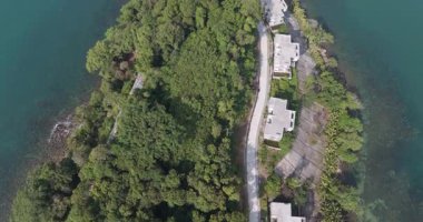 Havadan aşağıya tamamlanmamış beton villalar, yoğun tropikal orman ve bir adada asfalt yol..