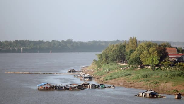 Vista del puente a casas flotantes a lo largo de la orilla del río y gente caminando por el sendero que conduce desde el muelle hasta la ciudad — Vídeos de Stock