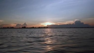 Günbatımında açık gökyüzü altında bir göl kenarında bir yolculuğu sırasında küçük bir motorlu tekne görüntülemek