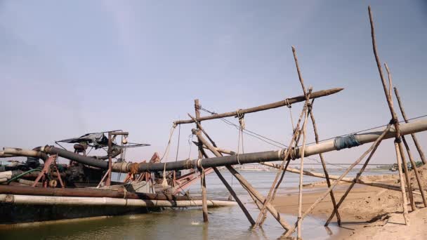 Дренажная лодка у берега реки с трубопроводной системой удерживается с бамбуковыми столбами для сброса выкопанного речного песка — стоковое видео