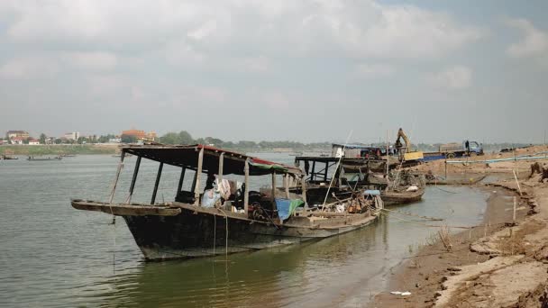 Barcazas de madera atadas a la orilla del río. Excavadora de descarga de arena de río dragado de una barcaza en un camión como telón de fondo — Vídeo de stock