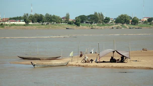 Fishers sitting under tarpaulin on river sandbank during windy day — Stock Video