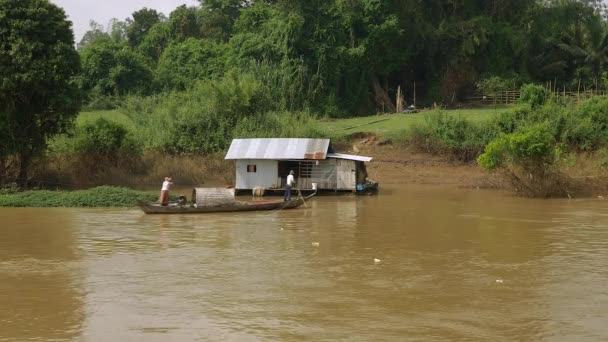 Husbåt på flodens kant och tropisk skog runt omkring; Liten fiskebåt förbi — Stockvideo