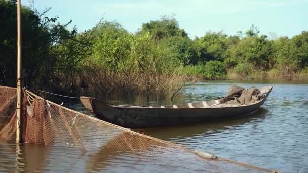Pequena canoa escavada amarrada ao poste de bambu e rede de pesca espalhada pelo rio — Vídeo de Stock
