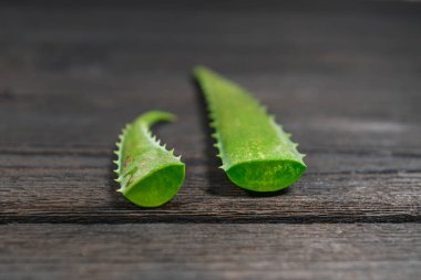 Aloe Vera yaprakları çapraz kesilmiş ve tahtalardan yapılmış koyu ahşap bir arka planda düzenlenmiş. Yaprağın iç kısmının jelatinimsi yapısını görebilirsiniz. Kesişen bölge nemli ve suyu akıyor..