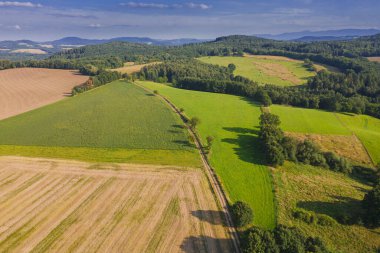 Sudeten etekleri. Çayırlarla, çayırlarla, ağaç kümeleriyle kaplanmış dalgalı bir arazi. Uzakta ufukta dağları görebilirsin. İHA 'dan fotoğraf..