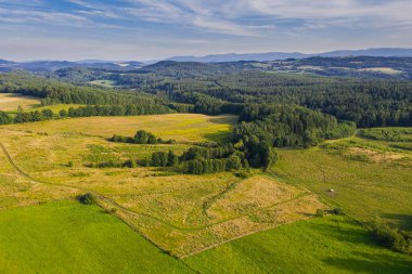 Sudeten etekleri. Çayırlarla, çayırlarla, ağaç kümeleriyle kaplanmış dalgalı bir arazi. Uzakta ufukta dağları görebilirsin. İHA 'dan fotoğraf..