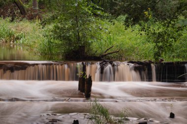 Küçük, dar, ovalı bir nehir. Nehrin karşısında bir eşik var, bir şelale oluşturuyor. Kıyılar çimen ve yeşil ağaçlarla kaplı..