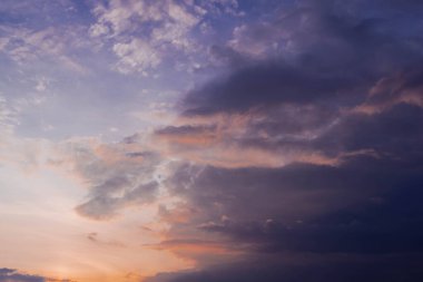 Otla kaplanmış düz bir arazi. Uzakta bir sıra ağaç var. Gökyüzü kısmen koyu bulutlarla kaplıdır. Batan güneşin ışığıyla kırmızıya boyanmıştır..