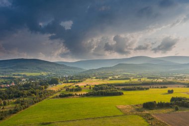 Ovadaki tarlalar ve çayırlar. Ufuktaki Karkonosze Dağları 'nın sisli zirveleri. İnsansız hava aracından görüntüle.