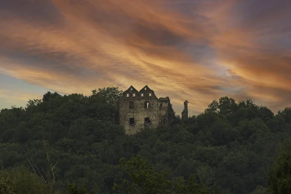 丘は落葉樹林で覆われている 上部には中世の城の遺跡の石壁を見ることができます 夜になると雲は赤くなる — ストック写真