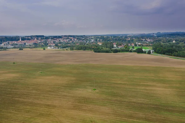 Geniş bir düzlük, yollarla geçen tarlalar ve çayırlar. Yeşil ağaç kümeleri görünür. Uzaktan yakındaki kasabanın binalarını görebilirsin. Gökyüzü hafifçe bulutlu. Fotoğraf İHA kullanılarak çekildi..