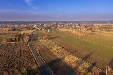 Tarlalarla, çayırlarla ve ağaçlarla kaplı bir ovanın içinden bir yol geçiyor. Güneşli bir gün. Fotoğraf İHA kullanılarak yüksek irtifada çekilmiş..