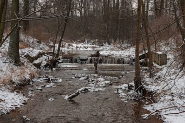 Ormanda akan küçük bir nehirde bir şelale. Kış mevsimindeyiz, nehir kısmen donmuş ve zemin bir kar tabakasıyla kaplı..