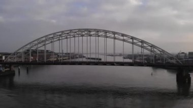 Bulutlu bir günde Hollanda nehri Noord 'da dönen bir mavnayla, arka planda Bascule Köprüsü' nde giden arabalar ve bir kamyon. Yaya aracı atışı.