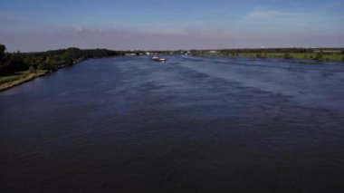 Hollanda 'nın Barendrecht kasabasındaki yeşil manzaralı Oude Maas Nehri' nde seyahat eden konteyner gemisi. hava durumu