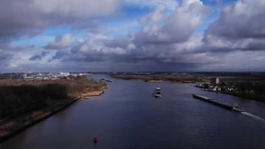 Hollanda 'da bulutlu gökyüzü olan Puttershoek kasabası yakınlarındaki Oude Mass nehrinde yelken açan yük ve yük gemileri. - Havadan Geniş Atış
