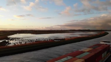Tam donanımlı kargo gemisi Hollanda nehri Noord 'da konteynırlarla denize açılırken güneş arka planda parçalı bulutlu bir kış gününde altın bir parıltı veriyor. Geniş açıyla.