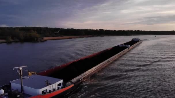 貨物に石炭を搭載した爆発性のばら積み貨物船は オランダのサウスホランド州バレンドレヒト近くの夕暮れ時に穏やかな川を航行しています 空中射撃 — ストック動画