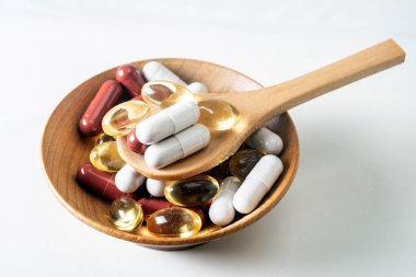 Tahta bir kasede bambu kaşıkla farklı haplar ve kapsüller. İzole edilmiş beyazı kapat