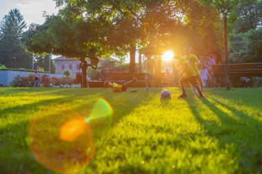 Odaklanamamak, bulanıklaşmak çocuklar, parkta güneş batarken çimenlerde futbol oynamak. Lens ve sarı ışık da mevcut. 