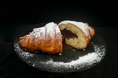2 parça çikolatalı kruvasan, şekerle pudralanmış, siyah arka planda izole edilmiş, siyah taş bir fayans üzerinde.. 