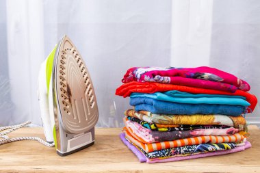 Renkli, katlanmış çamaşır ya da eşarpların yanında yanık izleri olan ütü.