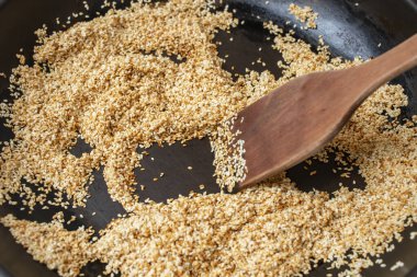 Kahverengi susam tohumlarını ahşap bir spatulayla karıştırıp kızartıyorlar. Tahini yapım süreci.