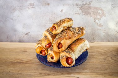 Evde ahşap bir tahtanın üzerinde hamura sarılmış sosisler, mavi bir tabakta yığılmış fast food.